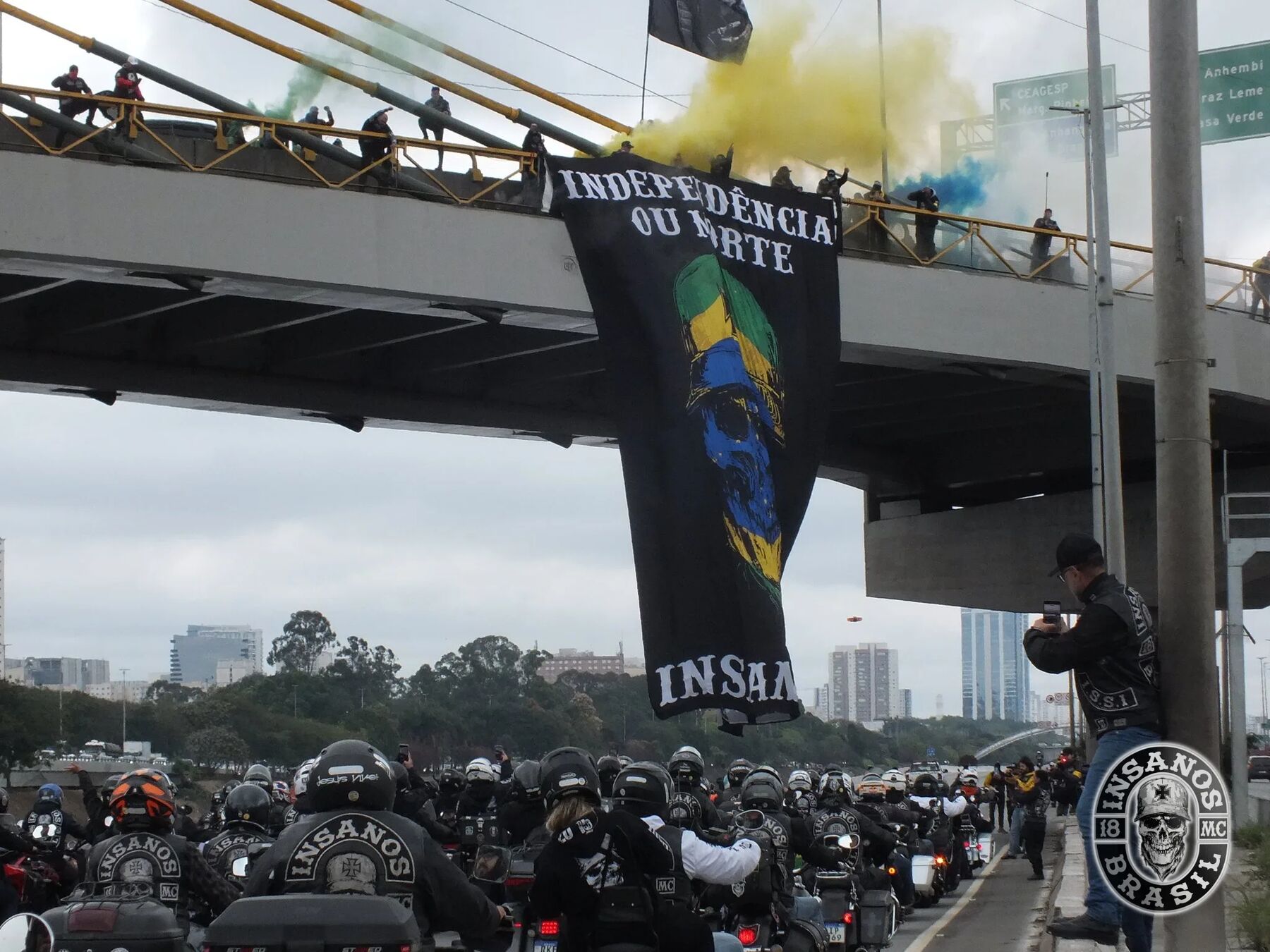 Faixa Independência ou Morte pendurada no viaduto sobre a Marginal, com o bonde do Insanos MC passando embaixo
