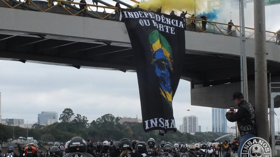 Faixa Independência ou Morte pendurada no viaduto sobre a Marginal, com o bonde do Insanos MC passando embaixo